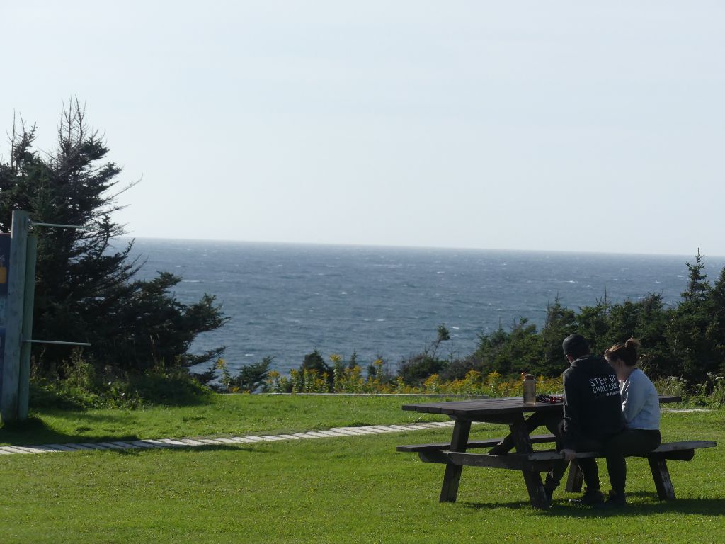 Two people sitting at a picnic table by the ocean