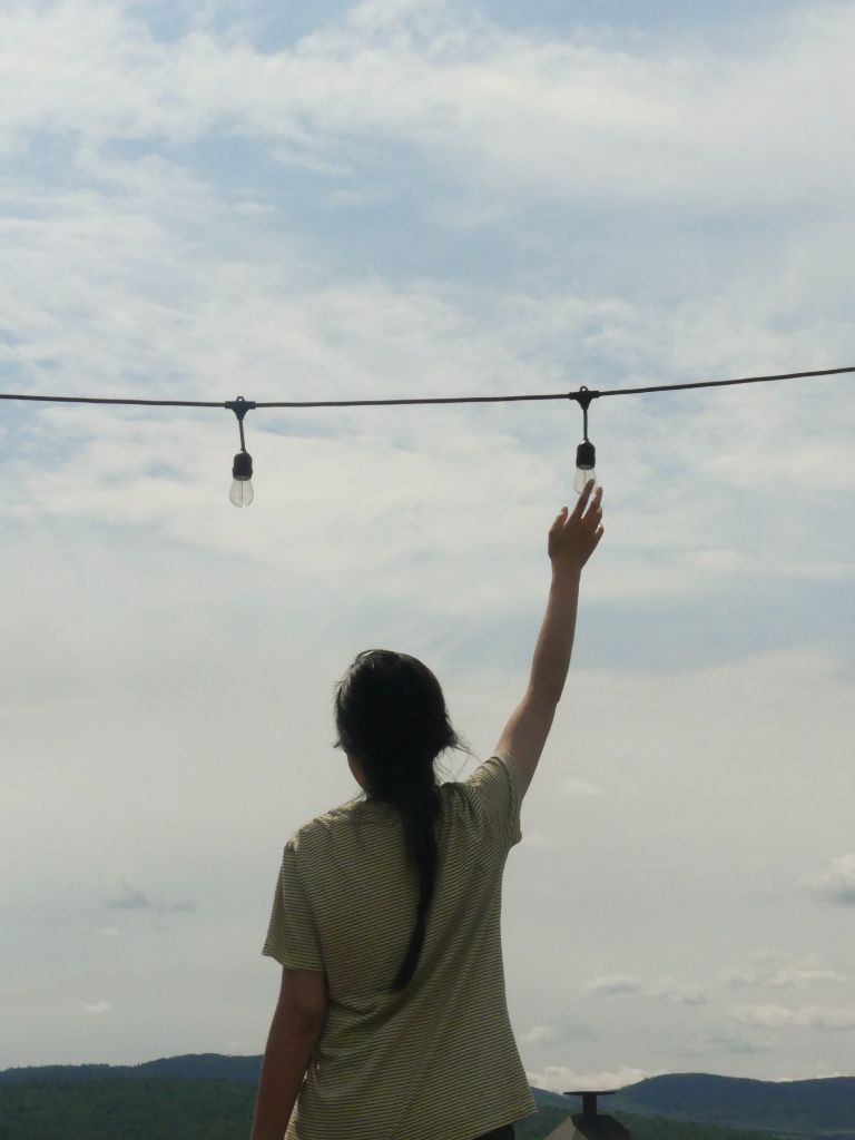 Person reaching for light bulb against sky